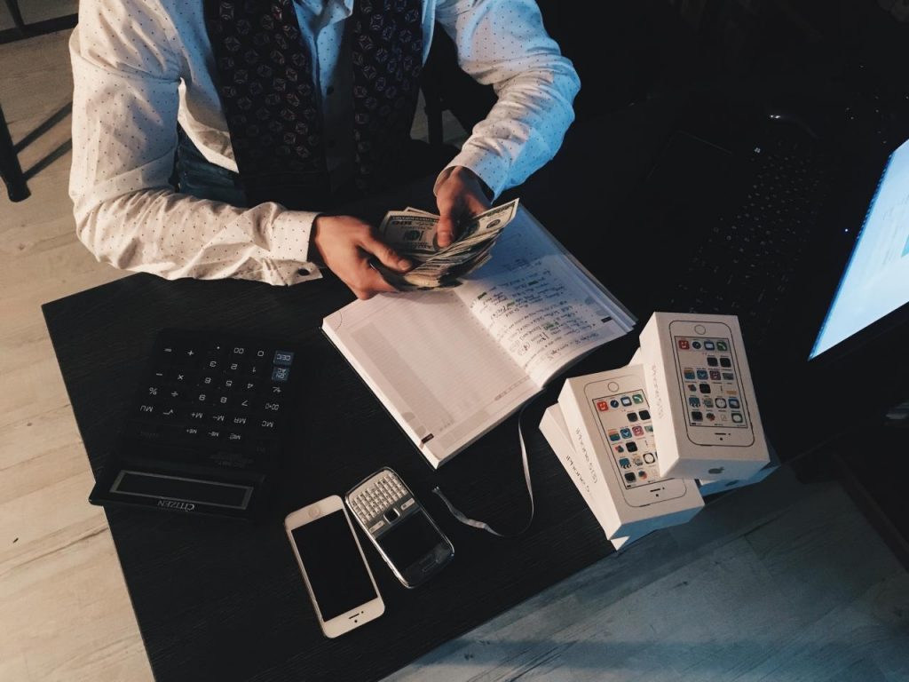 person counting money with smartphones in front on desk 3
